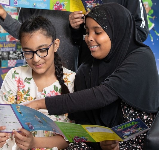 Two girls sitting in a library looking at a space themed booklet