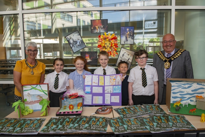 Five young people standing at a desk proudly displaying their art work. Town officials stand on either side; a man and a woman