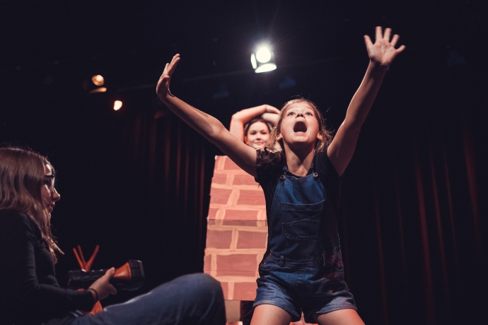 A young person performing on stage shouting with their arms raised 