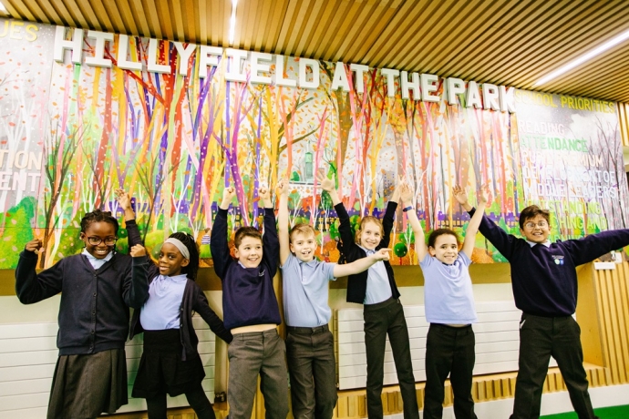 Children standing in front of a colourful wall mural with their arms raised in the air.